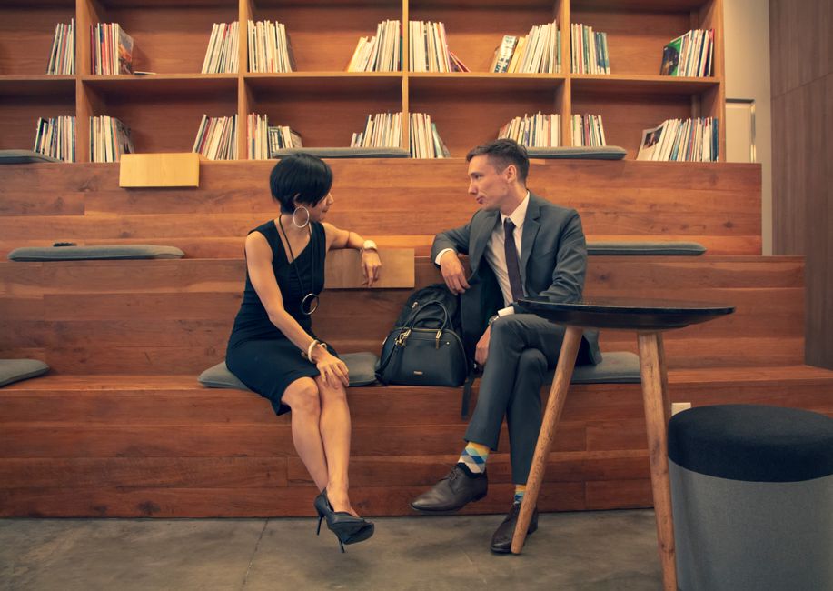 Professionals conversing in a stylish library, seated on wooden benches with bookshelves in the background.